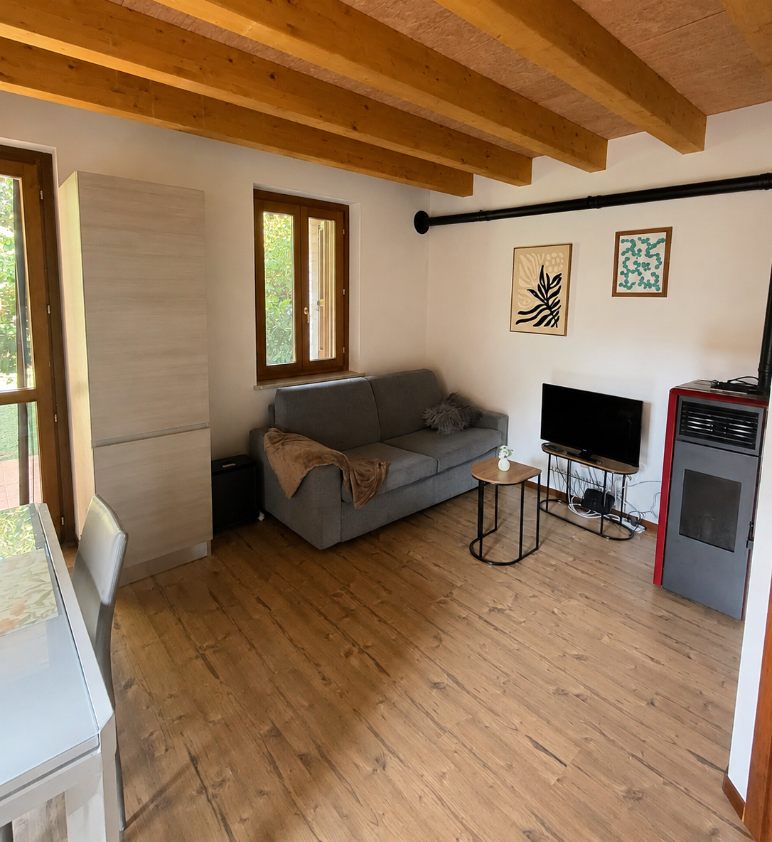 Soggiorno con divano, televisione, stufa e soffitto con travi in legno